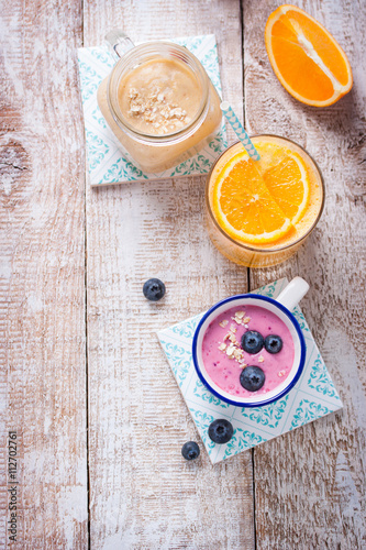 A mix of three smoothies with blueberry, orange and peach on a wooden background with copy space, top view