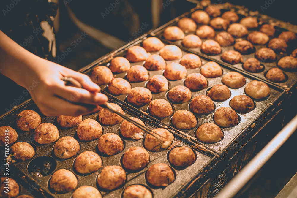 Takoyaki, Japan's famouse appetizer Takoyaki showing seller using chopstick  flipping piece Stock Photo