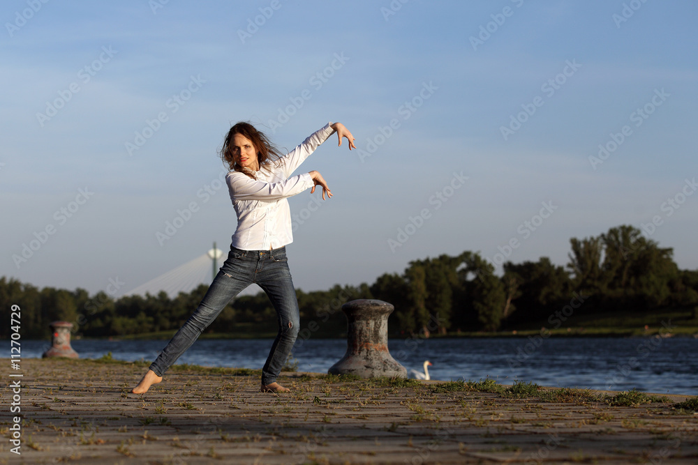 Beautiful young woman dancing at a river in evening light