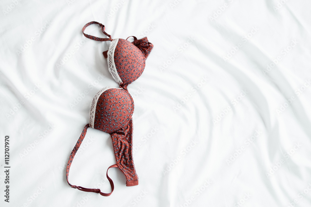 Red bra on white bed top view. Close-up of red female brassiere lying on  white bed. Beautiful part of women lingerie on white textile crease  background Stock Photo