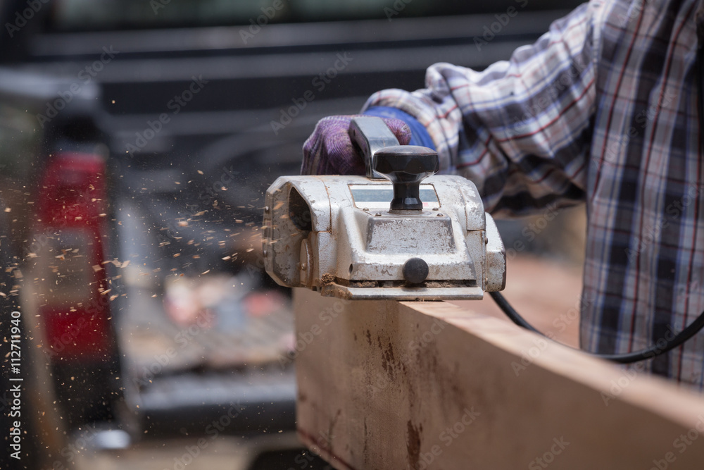 worker planing a wood with a electric plane