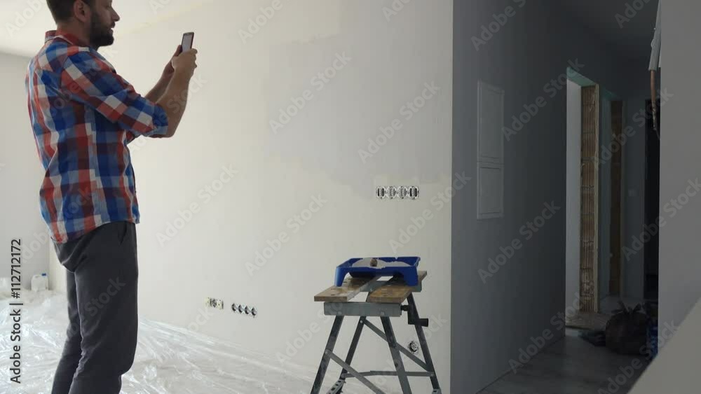 Young man painting wall and taking photo with cellphone at his new home
Young man painting wall and taking photo with cellphone at his new home