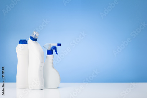 House cleaning products on white table with blue gradient backdrop. Lots of copy space around objects.