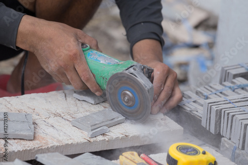 worker cutting a sand stone tile using an angle grinder