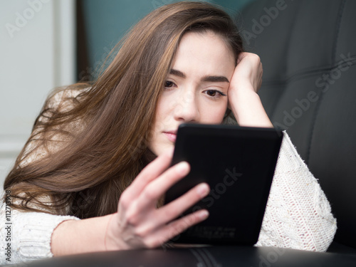 Εκτύπωση καμβά Girl reading e book on the sofa at home.