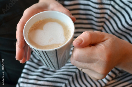 Woman holds a mug with coffee in a shape of a heart