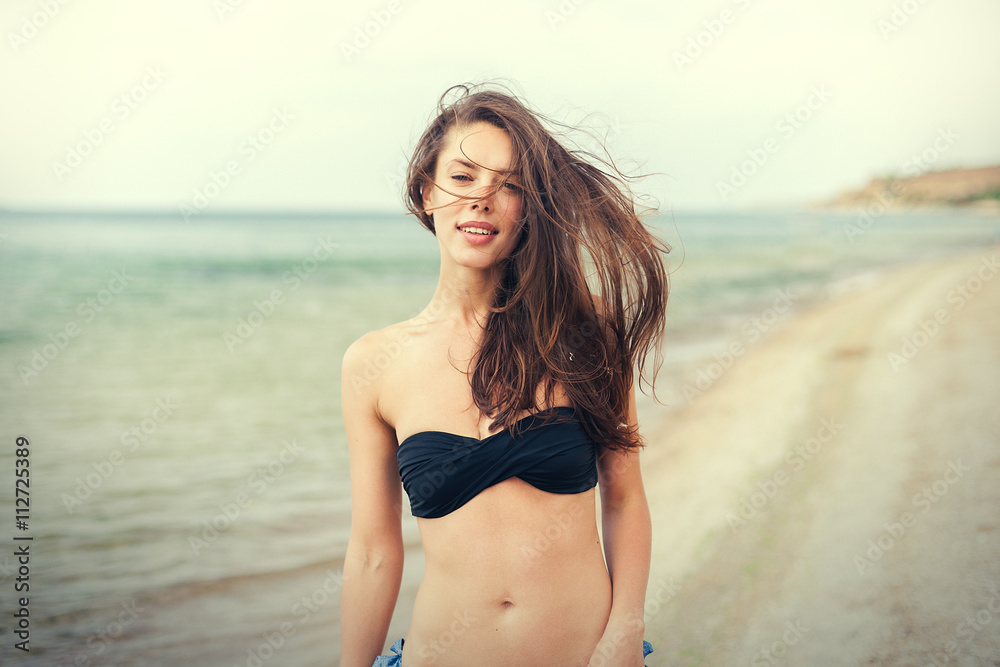 young smiling woman in black bikini on sea background young smiling woman in black bikini on sea background