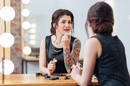 Beautiful tattooed woman applying lipstick in dressing room