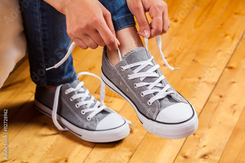 Girl wearing a pair of sneakers at home. A sneaker is untied