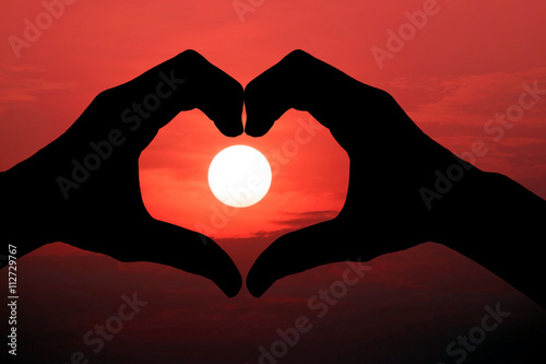Silhouette of hand made heart symbol across the sun was falling.