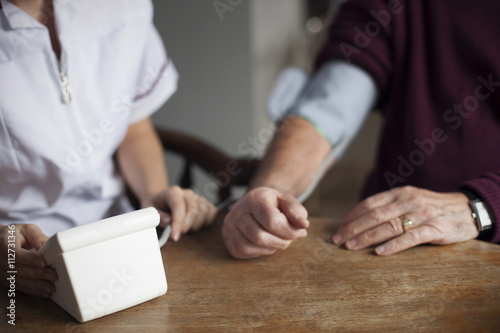 Nurse Taking Senior Man's Blood Pressure At Home