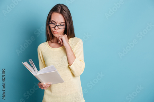 Beautiful pensive young girl reading book over blue background