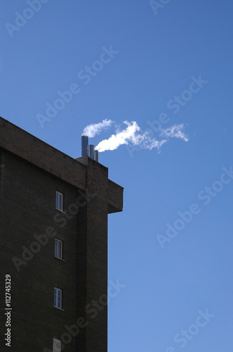 Edificio silueteado sobre cielo azul con humo photo