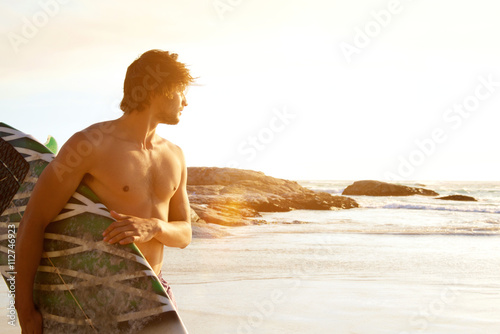 Young surfer standing by sunset
