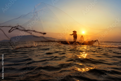 Silhouette of traditional fishermen throwing net fishing lake at sunrise time.(The casting people living along the River) © weerasak