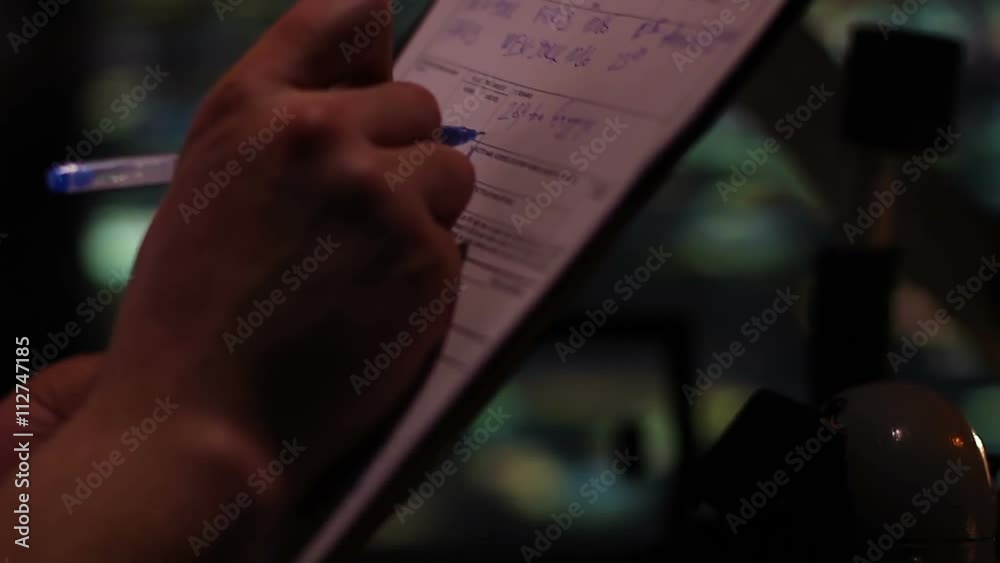 Pilot's hands writing in flight control papers, flying over night city, closeup