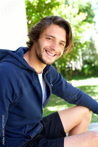 Smiling young man sitting outside © mimagephotos