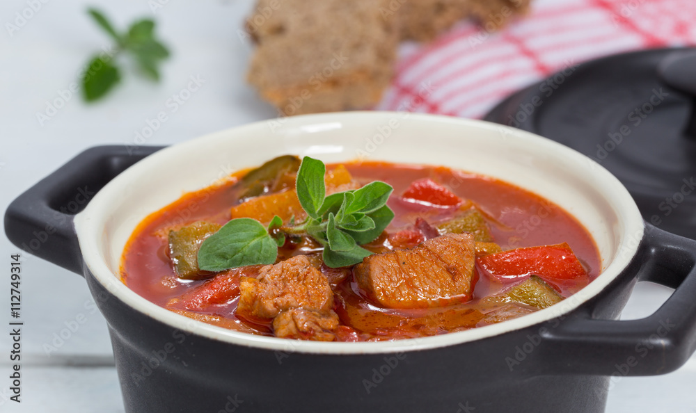 Gulasch in einer schwarzen cocotte mit Majoran auf weißem Holz Gulasch in einer schwarzen cocotte mit Majoran auf weißem Holz