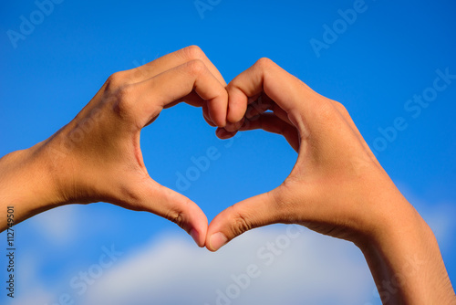 Girl hands in shape of love heart on blue sky with cloud.
