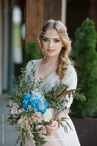 портрет невесты крупным планом с букетом в руках в стиле бохо и украшением на волосах заплетенных в косу которая стоит на открытой веранде