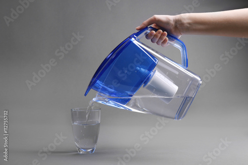 A hand pouring filtered water in the glass, on the grey background