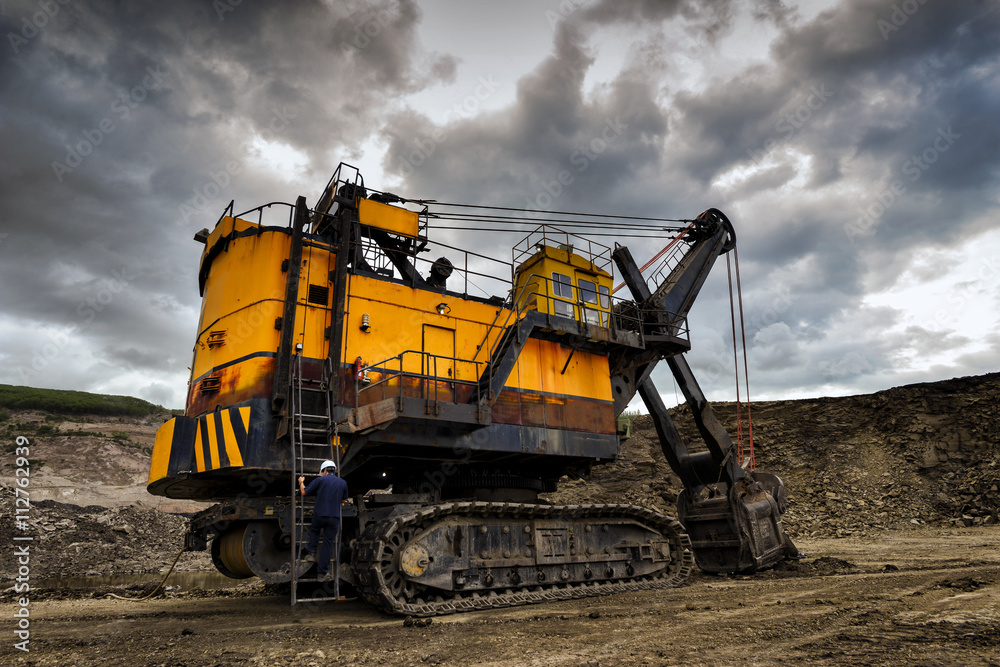 Yellow excavator loading soil on a truck at mine back lit