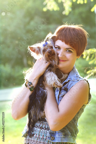 Beautiful young happy woman holding small dog in summer day walks in park
