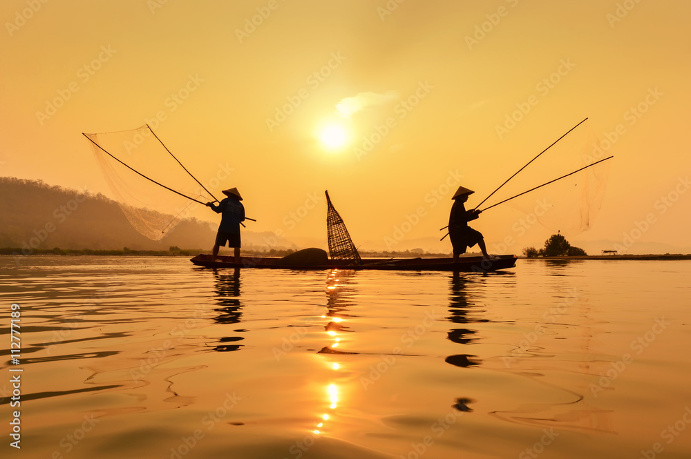 Siluate fisherman casting a net into the water during on the mist at sunrise