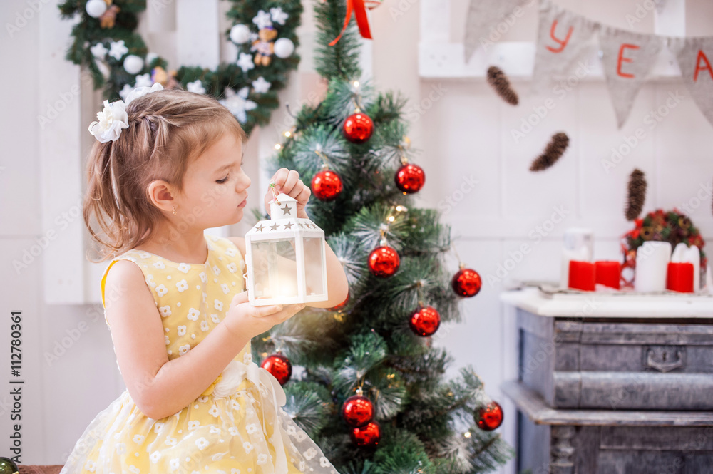 girl in yellow dress in front of tree holds the Christmas lantern