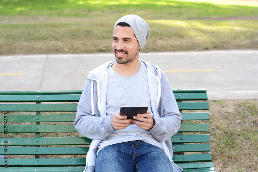 Obraz premium Young man using tablet sitting on park bench.