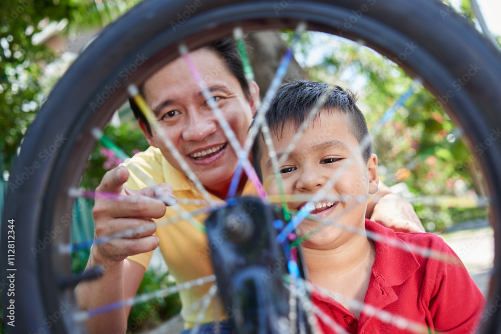 Cheerful Asian father looking at spinning wheel of bicycle Cheerful Asian father looking at spinning wheel of bicycle