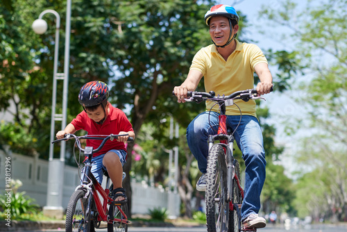 Vietnamese father and son in helmets cycling in the city © DragonImages