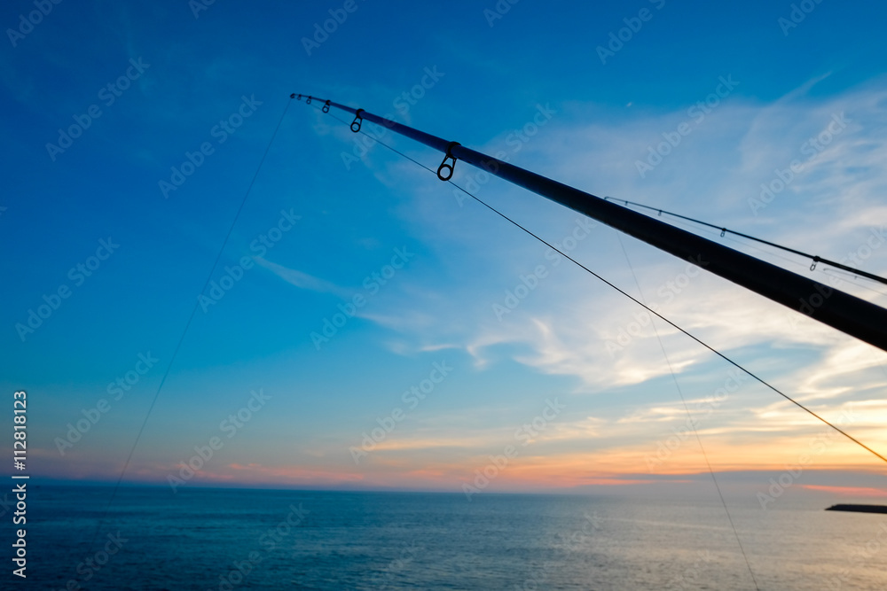 The silhouette of fishing poles under dramatic sunset and beautiful sea