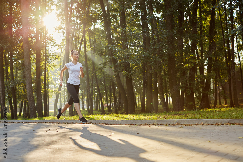 Fototapeta premium Attractive young woman running in park during sunny morning