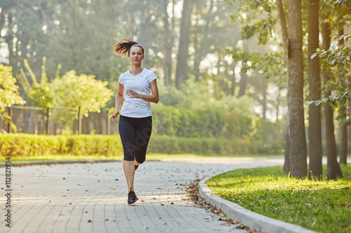 Young woman running in park at sunny summer morning photo