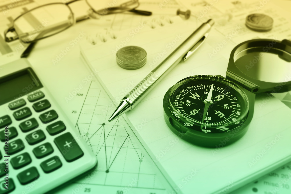 Compass, pen, glasses and coin on notebook, accounting backgroun Compass, pen, glasses and coin on notebook, accounting backgroun