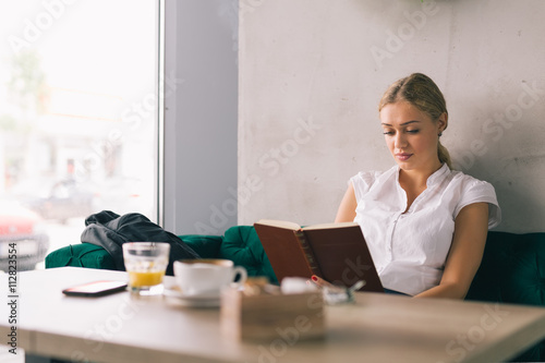 Enjoyoing coffee break. Woman reading book in cafeteria photo