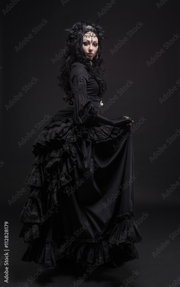 Fatal woman in vintage black dress posing on dark background
