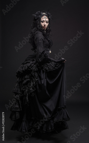 Fatal woman in vintage black dress posing on dark background