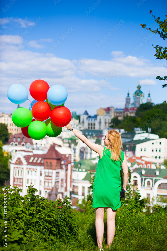 Happy young woman in green dress holding colorful balloons and flying over a panorama of old Kiev, Ukraine