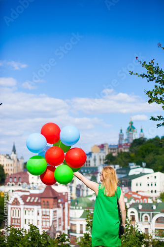 Happy young woman in green dress holding colorful balloons and flying over a panorama of old Kiev, Ukraine