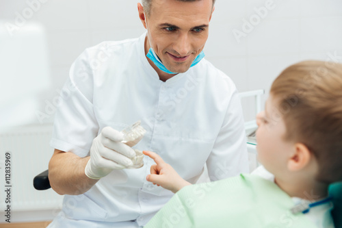 Fotografie Smiling man dentist showing dental jaw model to little boy