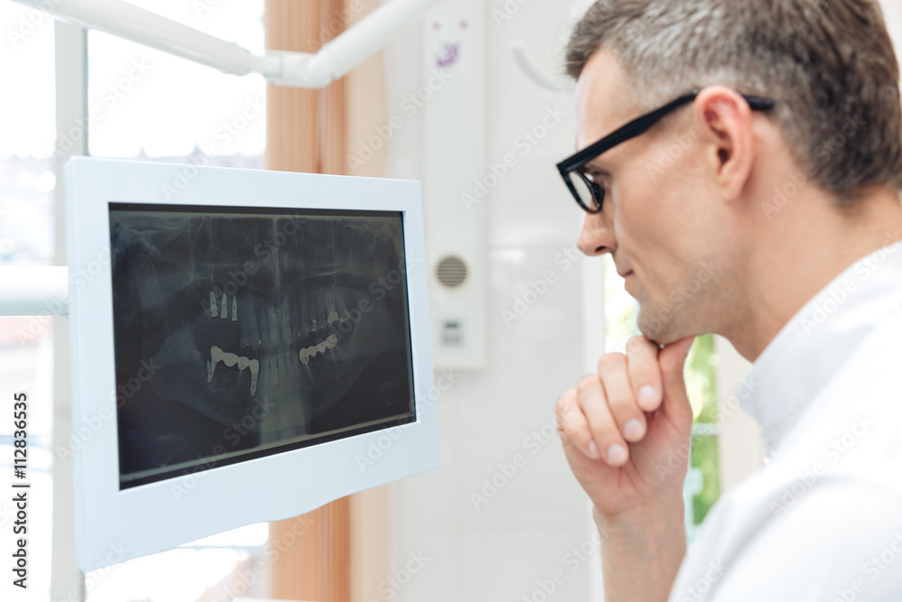 Fototapeta premium Male dentist looking teeth on digital X-Ray computer monitor
