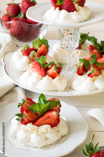 Homemade small strawberry pavlova meringue cakes with mascarpone cream and fresh mint leaves on white plate