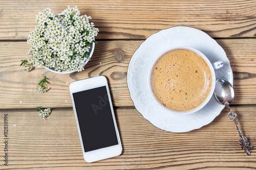 Cup of coffee, mobile phone and flowers on wooden table