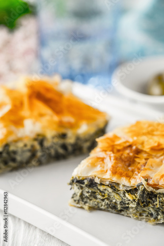 Greek pie spanakopita on the white plate with blurred accessorizes