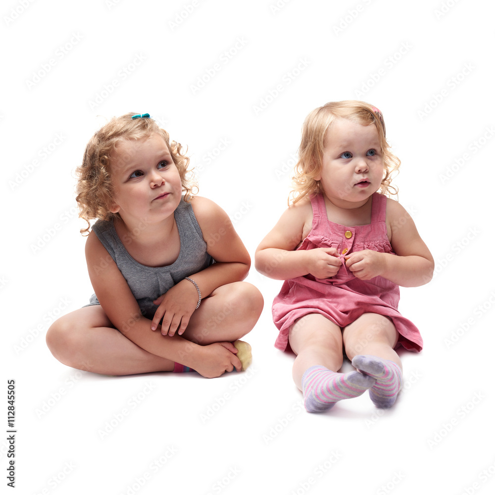 Couple of young little girl sitting over isolated white background Couple of young little girl sitting over isolated white background