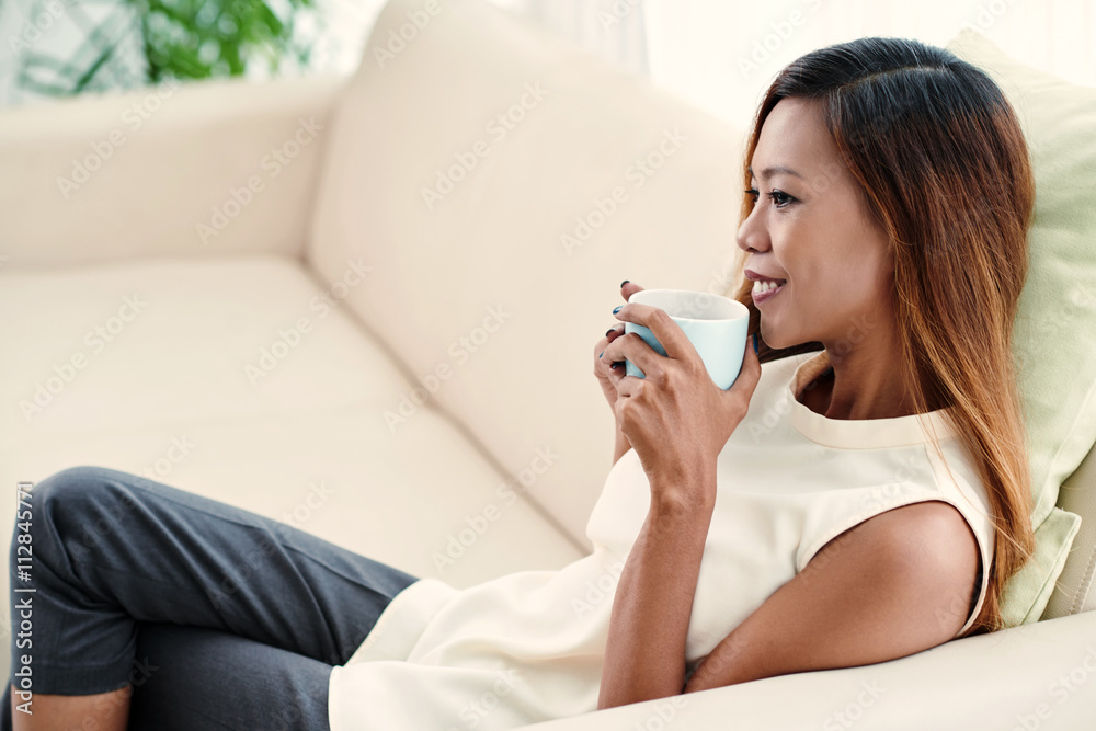 Charming young woman sitting on sofa with cup of coffee Charming young woman sitting on sofa with cup of coffee