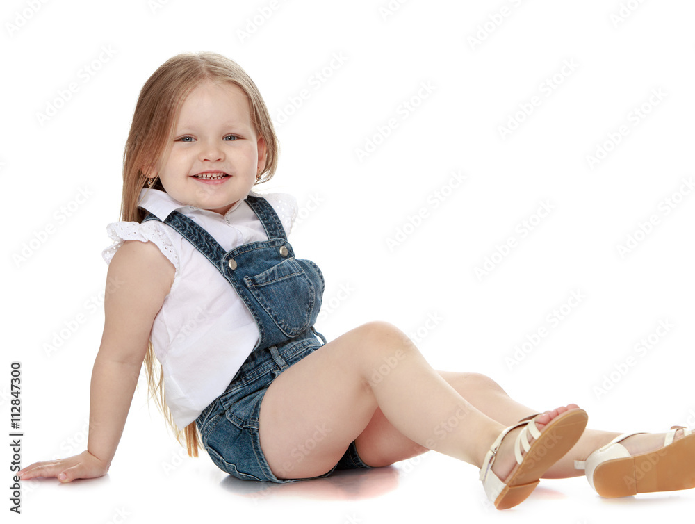 Laughing little girl with long blond hair in denim overalls