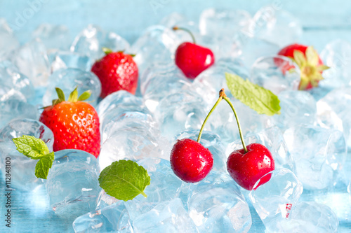Fruits in ice cubes with cherry and strawberry abstract food background 